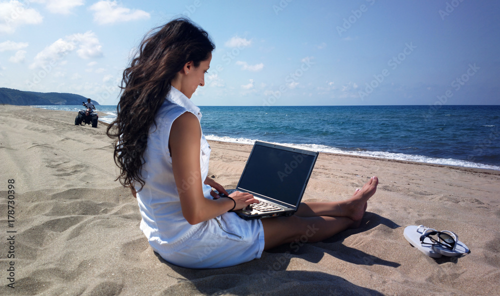 Young woman working on laptop by the sea