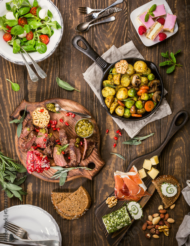 Flat lay of delicious dinner table with roasted meat steak, appetizers and desserts. Top view. Healthy food concept.