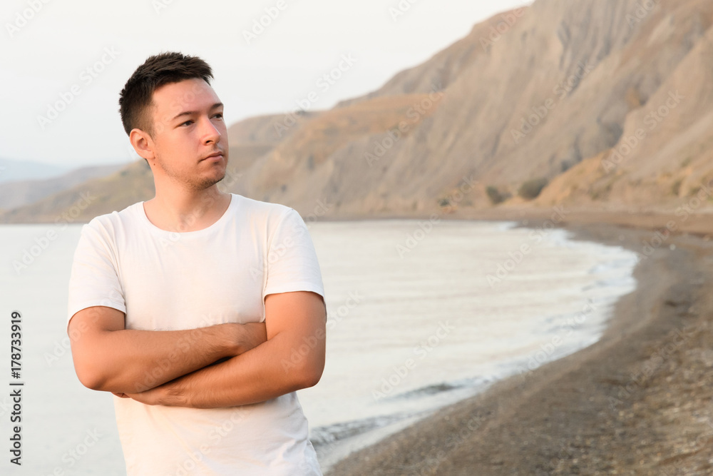 The young man looking towards the shore, arms crossed on his chest