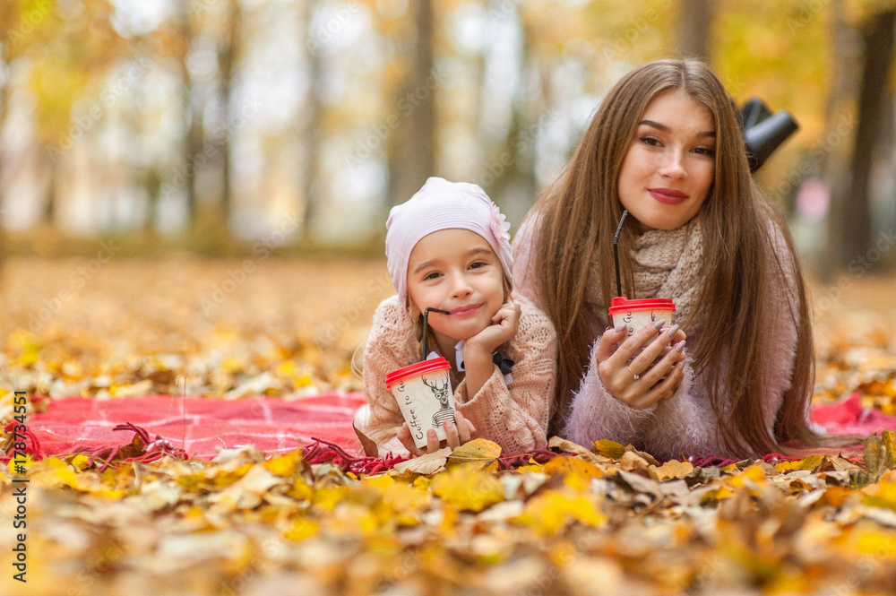 Beautiful mother and daughter lie in autumn leaves in a park or forest, drink coffee, tea or cocoa, communicate, laugh, have fun, mother's day Beautiful mother and daughter lie in autumn leaves in a park or forest, drink coffee, tea or cocoa, communicate, laugh, have fun, mother's day