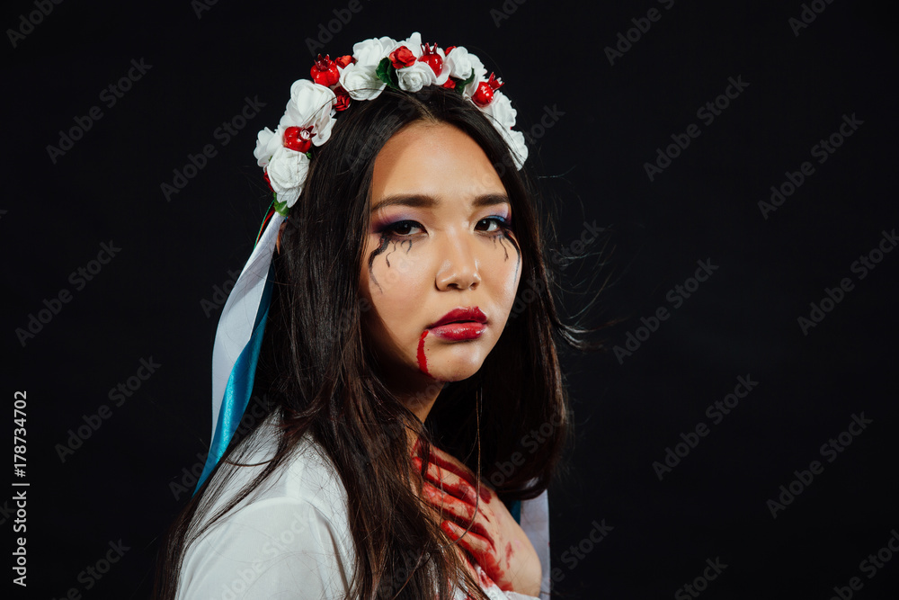 Portrait of a bloody beautiful Asian girl on Halloween. White dress-robe, ethnic wreath of flowers