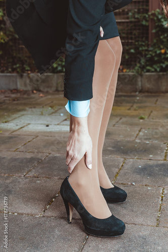 Woman in business dress and high heeled shoes holds painful ankle 