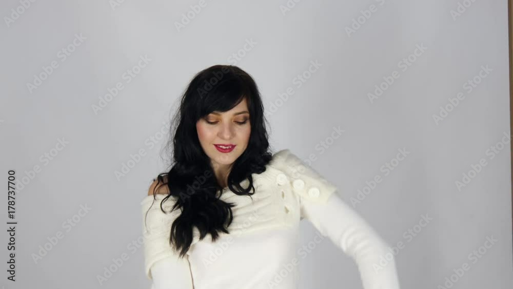 Young pretty black haired woman in white dress dancing and smiling on gray background.