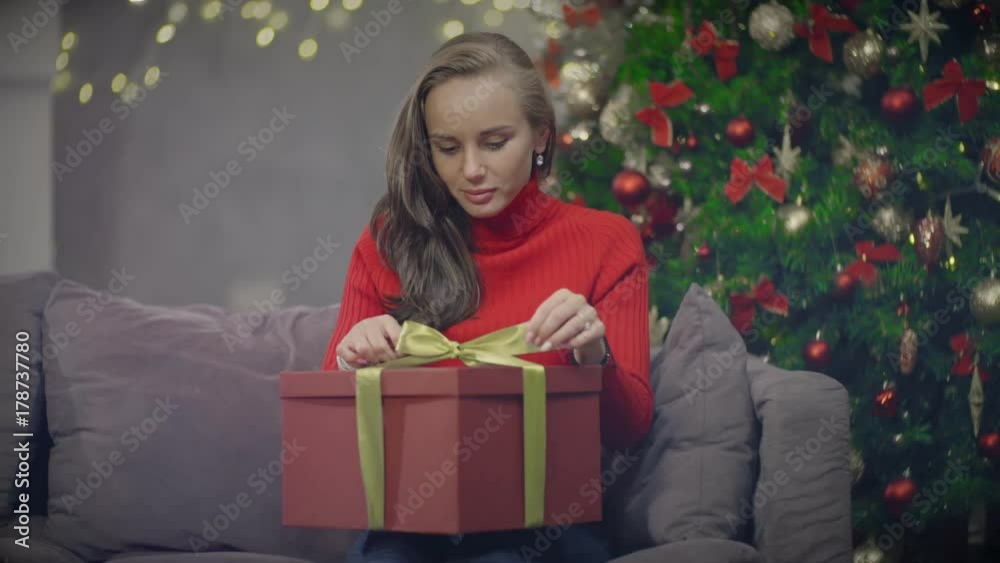 Beautiful woman sitting on couch and opening New Year present box Beautiful woman sitting on couch and opening New Year present box