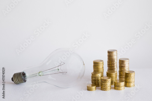 Old transparent glass light bulb with coins on the gray background. Electricity payment concept. Empty place for a text and other ideas.