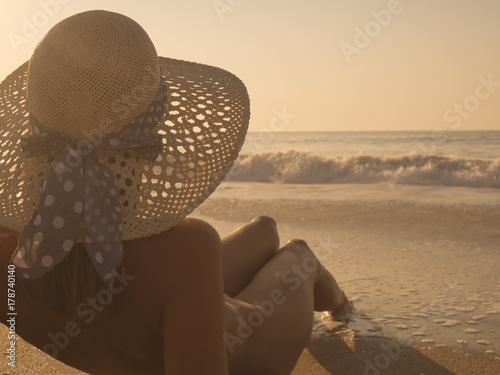 Nude Young fashion woman relax on the beach, sunbathing wearing only a hat