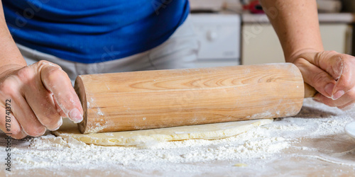 Girl rolls out the dough for a pie with a round rolling pin on the kitchen table