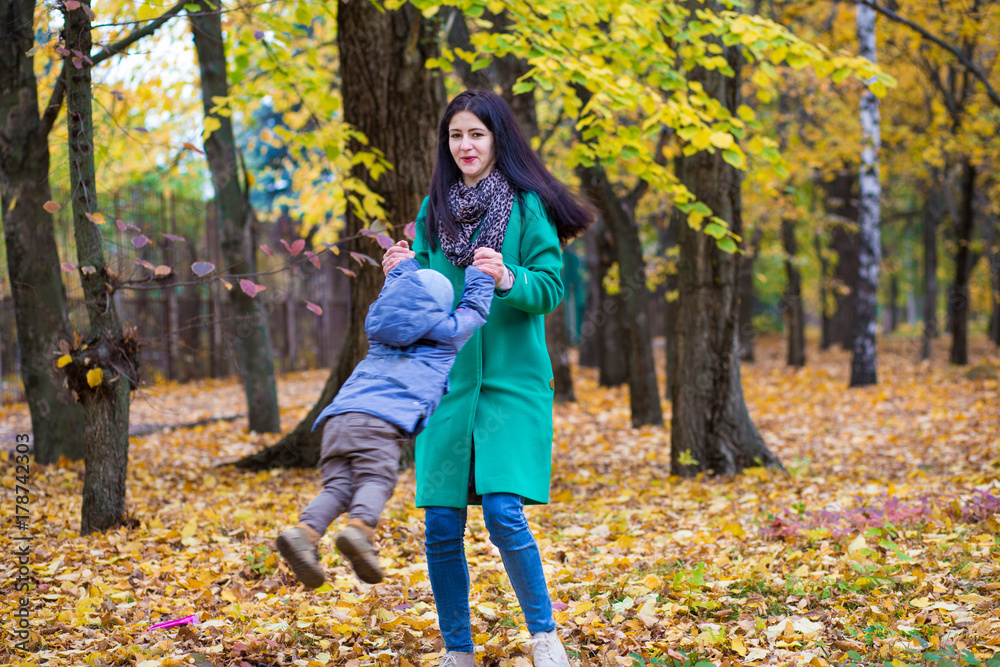 Mother with little son plays and smiles in park on background of colorful autumn fallen leaves Mother with little son plays and smiles in park on background of colorful autumn fallen leaves