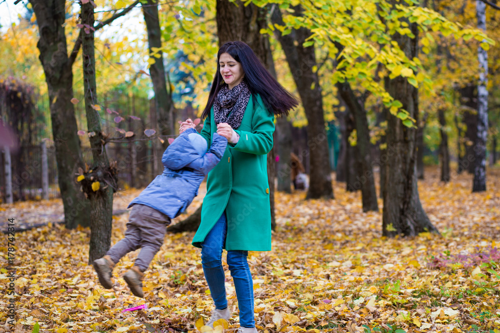 Mother with little son plays and smiles in park on background of colorful autumn fallen leaves Mother with little son plays and smiles in park on background of colorful autumn fallen leaves