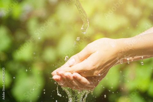 Woman washing hand outdoors. Natural drinking water in the palm. Young hands with water splash, selective focus. Instagram yellow effect.