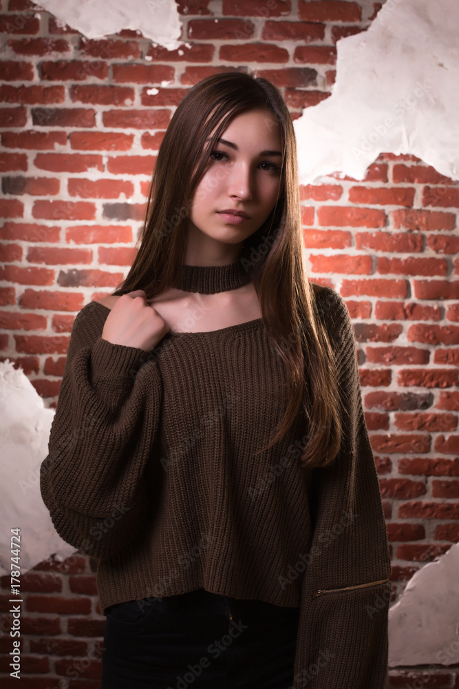 Naklejka premium Model test of fabulous brunette model with long hair, wears oversize sweater, posing on a brick wall background