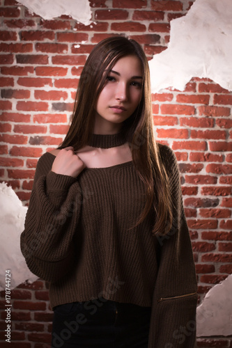 Model test of fabulous brunette model with long hair, wears oversize sweater, posing on a brick wall background