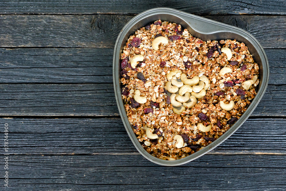 Granola with cashew in a heart-shaped baking dish. Black wooden table Granola with cashew in a heart-shaped baking dish. Black wooden table