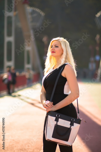 Magnificent blonde model with bright makeup, fashionably dressed, posing at the city