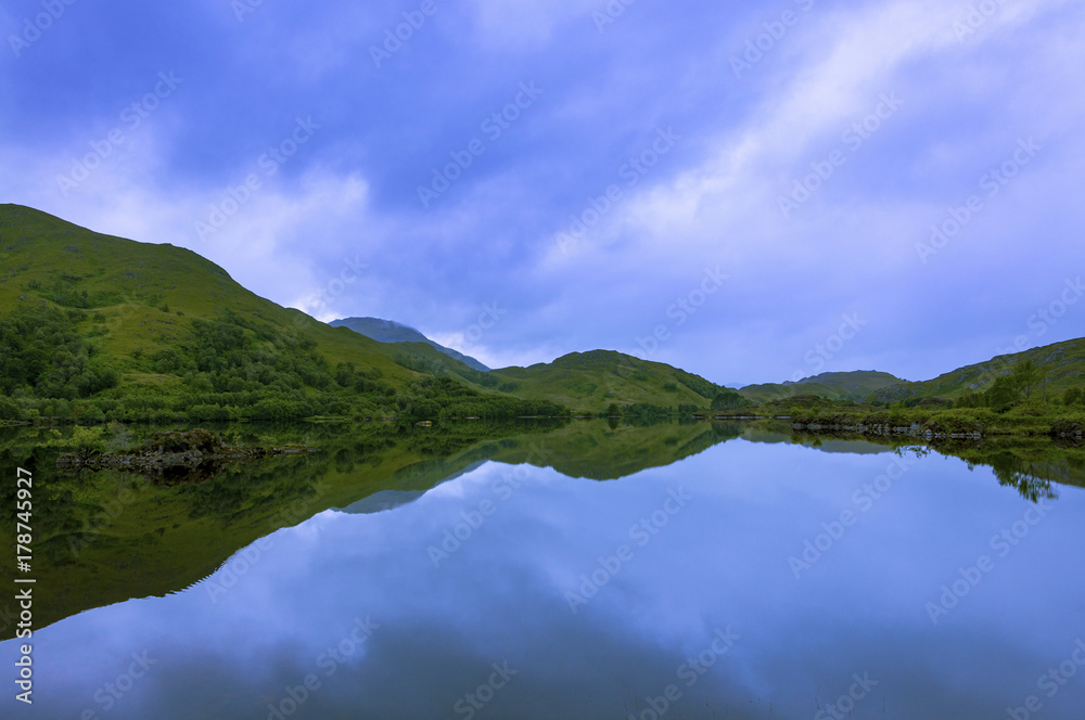 Beautiful and serene landscape of a lake and mountains in the Highlands of Scotland, United Kingdom; Concept for travel in Scotland Beautiful and serene landscape of a lake and mountains in the Highlands of Scotland, United Kingdom; Concept for travel in Scotland