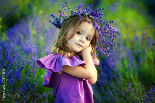 Cute smiling little girl with flower wreath on the meadow at the farm. Portrait of adorable small kid outdoors. Midsummer.