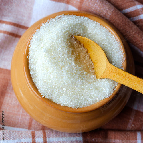 sugar loose in the bowl of a pot on a wooden table tablecloth in a cage. Wooden spoon. A rustic style. photo