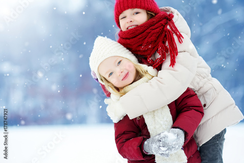 Two adorable little girls having fun together in beautiful winter park. Beautiful sisters playing in a snow.