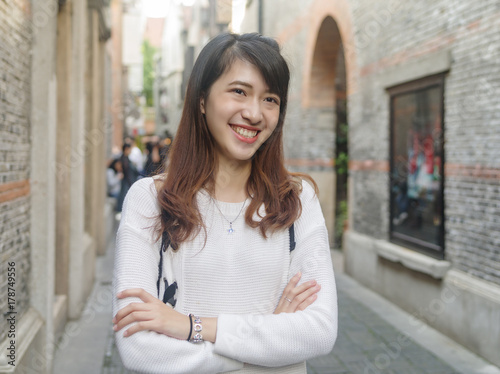 Portrait of beautiful young Chinese woman wearing white sweater and blue jeans in Shanghai Xintiandi, smiling with defocused Shikumen style street background, happy time , Asian girl Concept ,Travel C © atiger