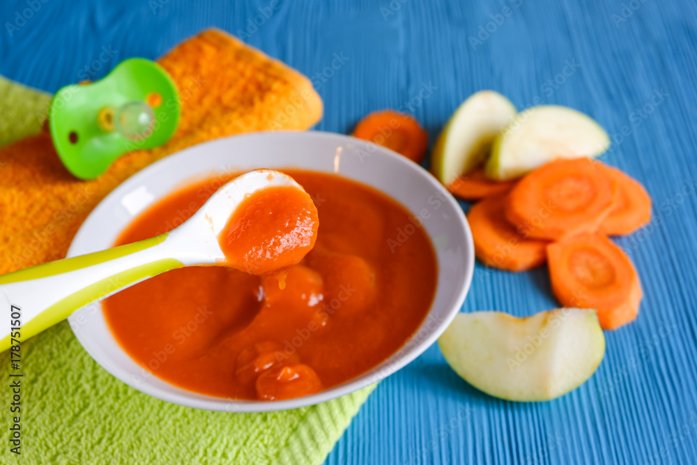 puree of baby carrot Apple on a wooden table spoon saucer white green pacifier napkin orange puree of baby carrot Apple on a wooden table spoon saucer white green pacifier napkin orange