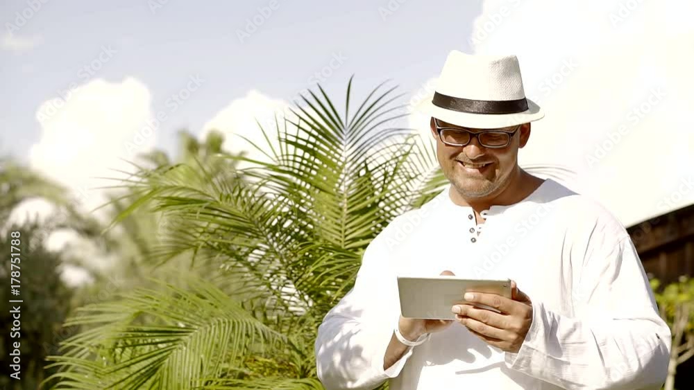 An adult man in glasses holds a tablet in his hand, the person looks through photos that were taken during the holidays An adult man in glasses holds a tablet in his hand, the person looks through photos that were taken during the holidays
