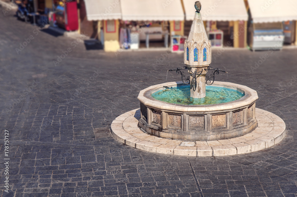 Beautiful public fountain in Rhodes town of Greek island with marble dark block street