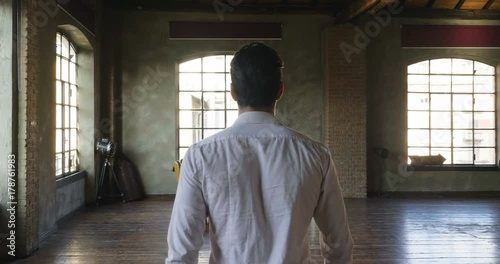 A handsome man in his loft dresses his sexy white shirt in a sexy way, looks into his room and smiles with a sure look at himself. Concept of: elegance, business, work....