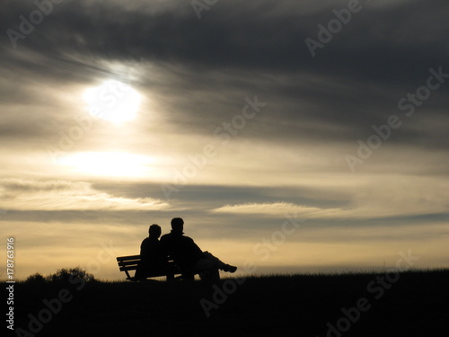 A Silhouette of a Couple Sitting on Park Bench at Sunset