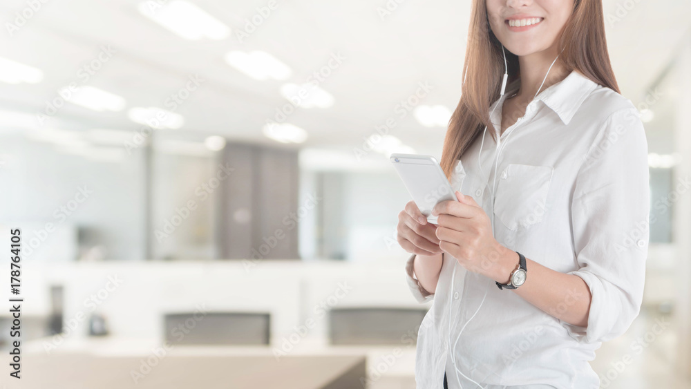 Beautiful young Asian girl using smart phone with earpiece in office space background and copy space.Concept of people using technology.