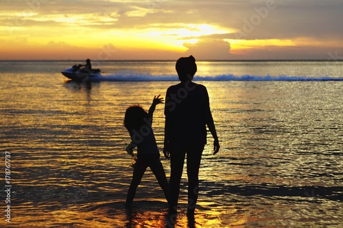 mother and daughter in silhouette against jet ski and beach during sunset