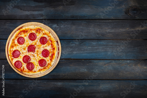 Classic pepperoni pizzai on a wooden stand on a dark wooden background. Top view orientation on the left side