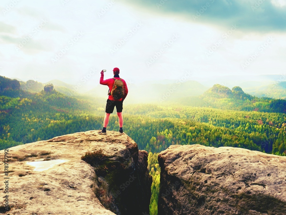 Obraz premium Mobile phone photographer. Tourist on the rocky edge take phone pictures. Hiking in mountains