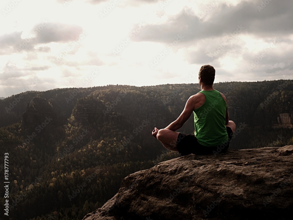 Man on top of mountain in yoga pose. Exercise yoga on edge with a breathtaking view