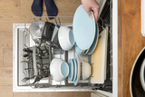 Overhead of an Open Dishwasher with Hand Placing Plate In