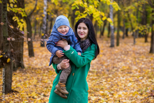 Mother with little son plays and smiles in park on background of colorful autumn fallen leaves