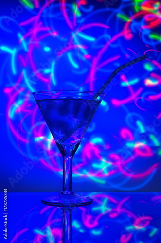 Glass with a straw cocktail with ice against a backdrop of abstract illumination of colored neon