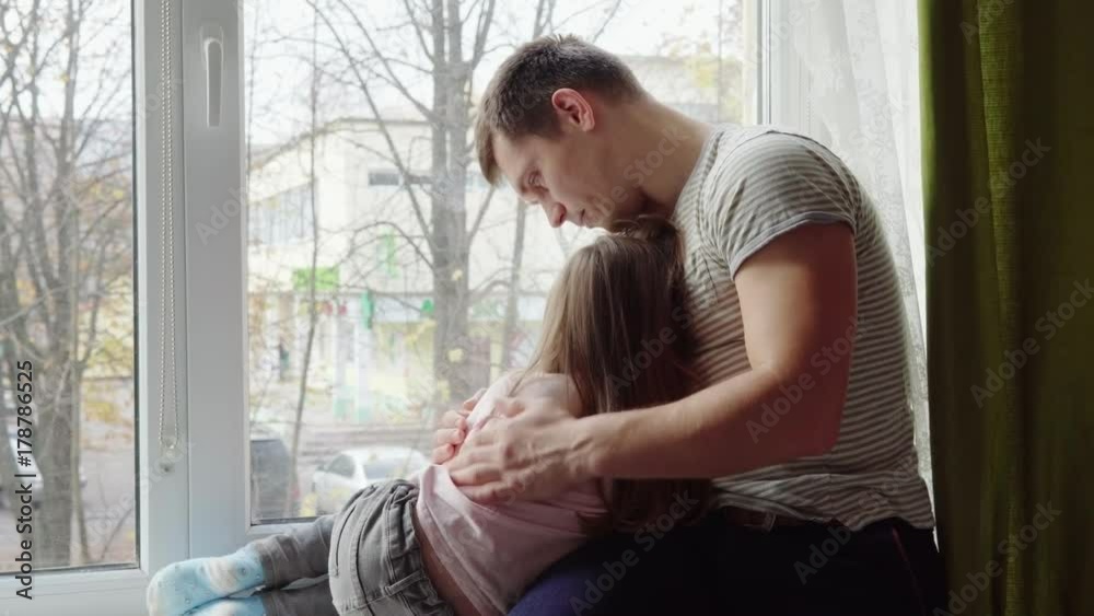 Father comforts his little daughter on the windowsill Father comforts his little daughter on the windowsill