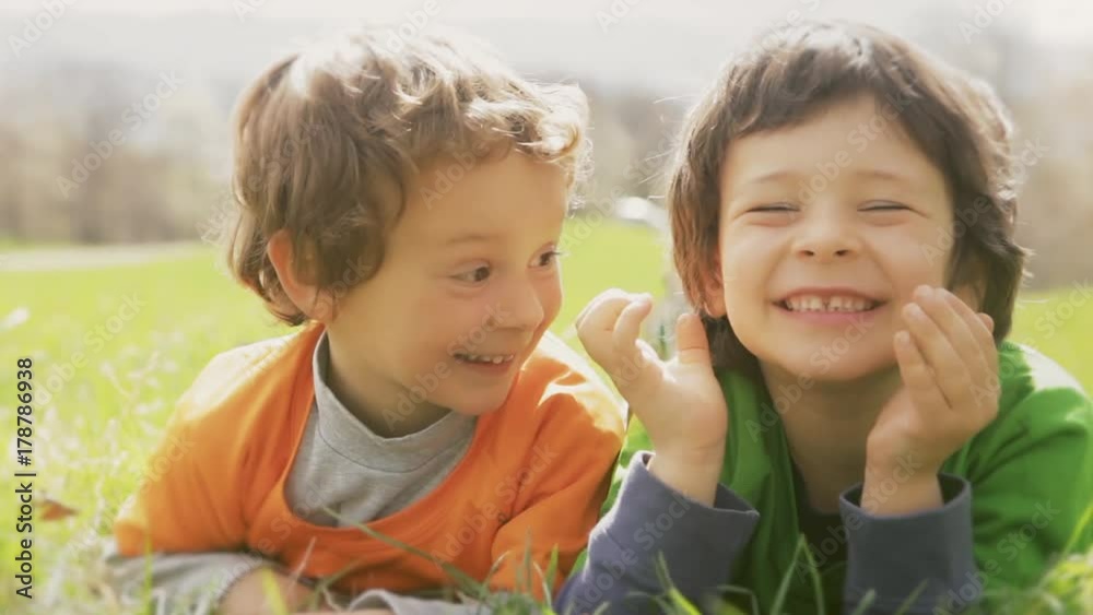 Happy children smiling close up portrait. Two brother kids laughing and playing while lay down on grass meadow in outdoor sunny day. Family son boys relaxing in nature.video footage Happy children smiling close up portrait. Two brother kids laughing and playing while lay down on grass meadow in outdoor sunny day. Family son boys relaxing in nature.video footage