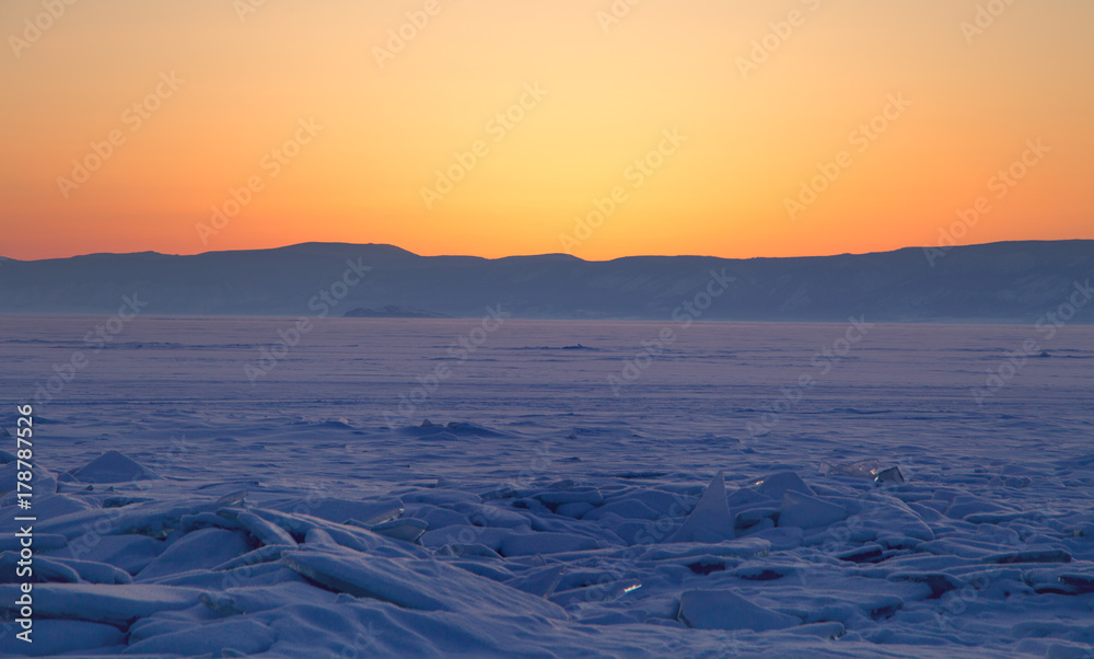 Transparent ice floe on a hummock field on the frozen Siberian Lake Baikal at sunset in winter.