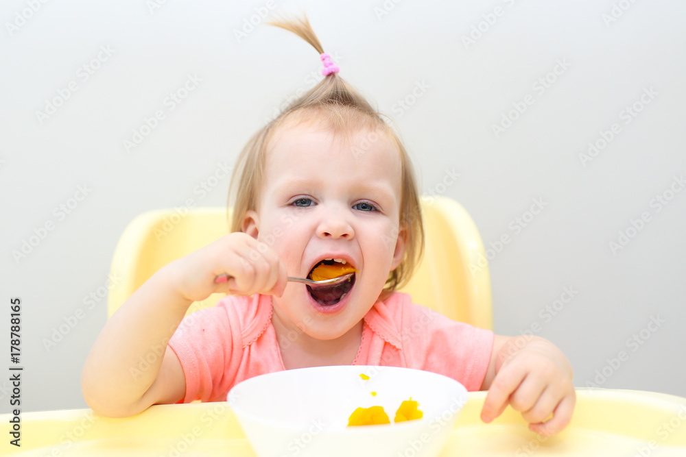 Happy lovely little 1 years girl eating pumpkin at home kitchen Happy lovely little 1 years girl eating pumpkin at home kitchen
