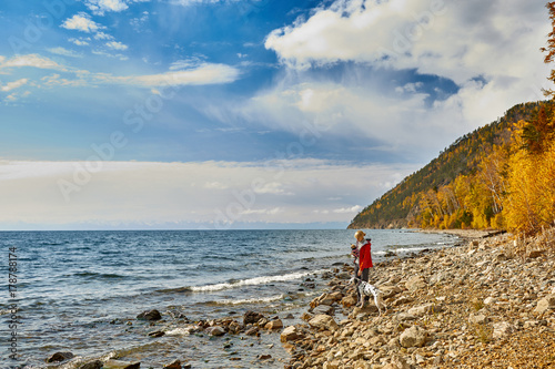The beautiful girl walks with dogs on the coast of the autumn lake