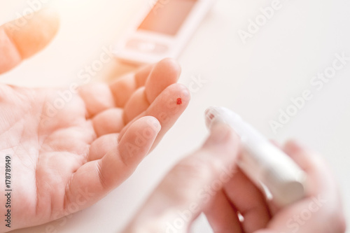 Medicine, diabetes, glycemia, health care and people concept - Close up of man hands using lancet on finger to check high blood sugar level with glucometer or glucose meter at home