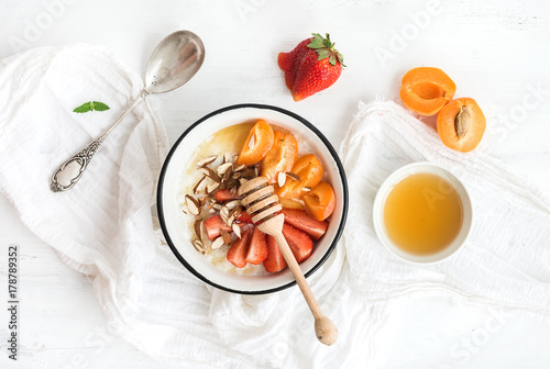 Healthy breakfast set. Rice cereal or porridge with fresh strawberry, apricots, almond and honey over white rustic wood backdrop, top view