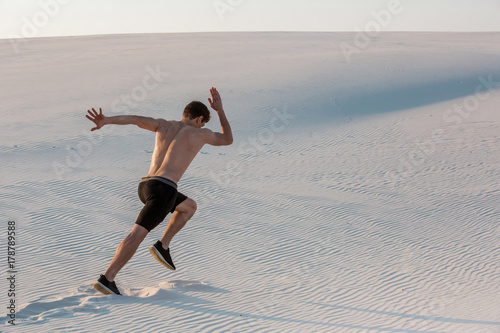 Fit man running fast on the sand. Powerful runner training outdoor on summer.