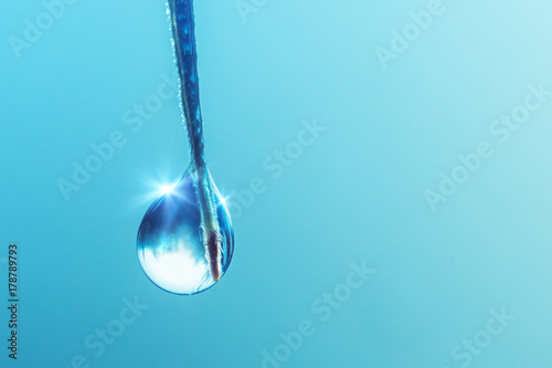 Drop of water  with a spark flowing down a blade of grass on a blue background