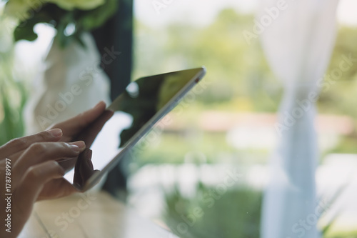 Closeup image of a woman's hands holding , typing and using tablet pc on wooden table in cafe