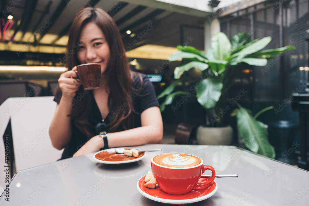 Closeup image of a beautiful Asian woman holding and drinking coffee with Americano coffee cup on glass table in loft cafe