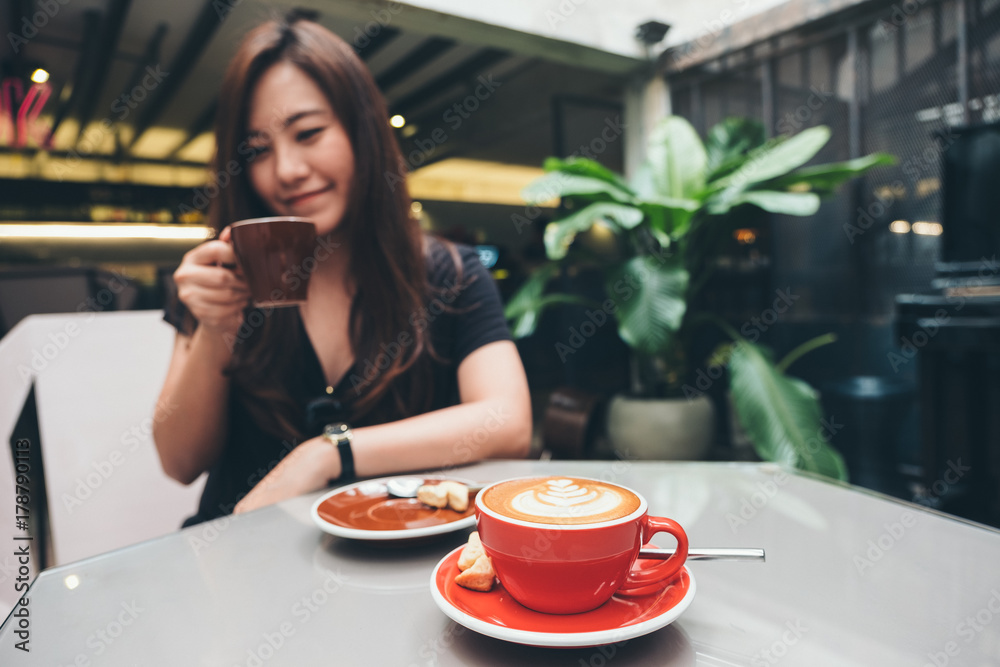 Closeup image of a beautiful Asian woman holding and drinking coffee with Americano coffee cup on glass table in loft cafe
