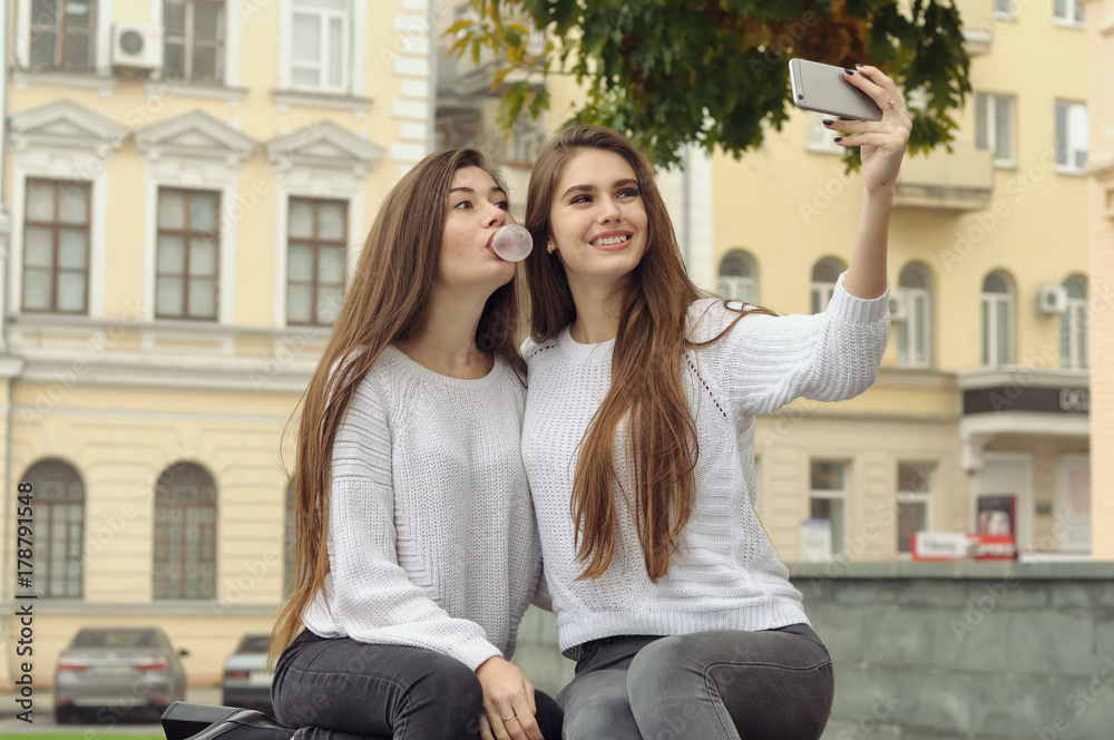 Two girlfriends puff bubbles out of chewing gum while they make a selfie photo Two girlfriends puff bubbles out of chewing gum while they make a selfie photo