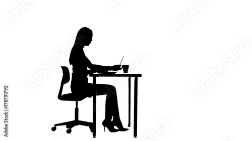 Girl uses a laptop and drinks tea at the table silhouette